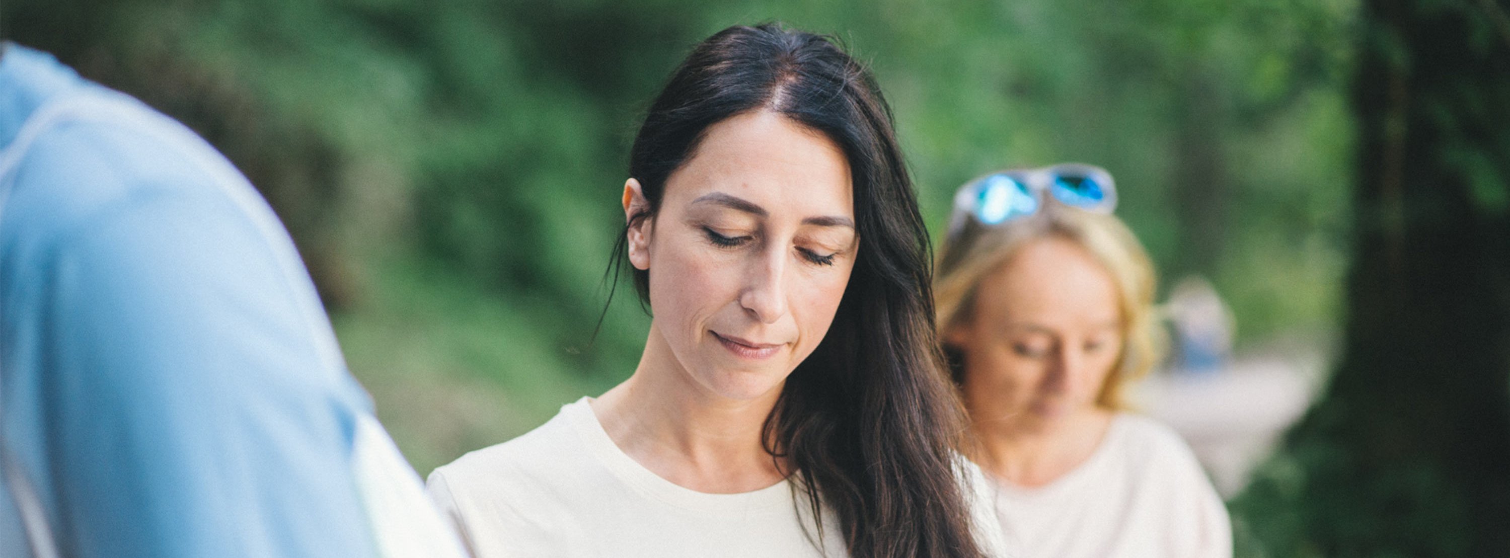 Drei Personen stehen draußen, im Hintergrund Bäume, und blicken auf ihr Handy.