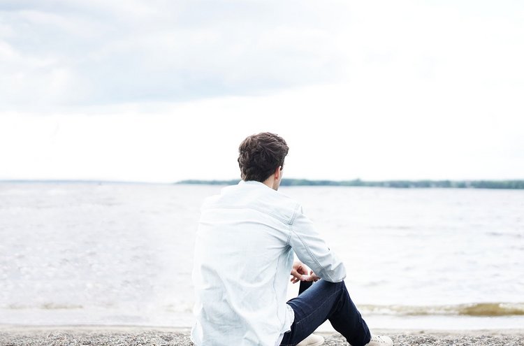 Mann sitzt am See und denkt nach