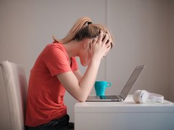 Frau blickt auf Laptop, schlägt Hände über dem Kopf zusammen