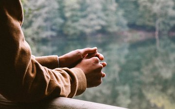 Burnout - Person, die sich an einem Geländer anlehnt mit einem See im Hintergrund 