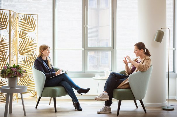 Zwei Frauen sitzen sich in hellgrünen Sesseln gegenüber und unterhalten sich