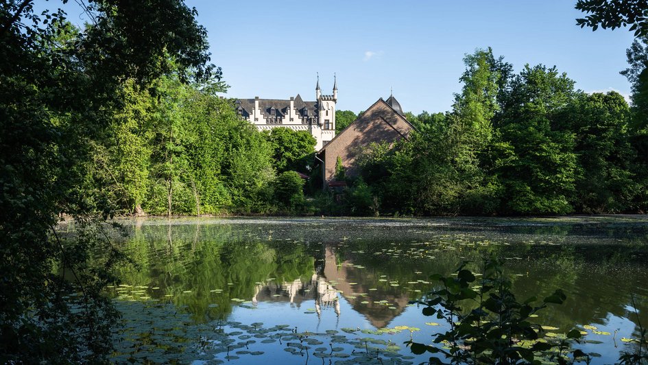 Malerischer Blick auf das historische Wasserschlösschen der Oberberg Kliniken, umgeben von üppiger Natur und einem idyllischen Teich mit Seerosen, der das Schloss im Wasser spiegelt