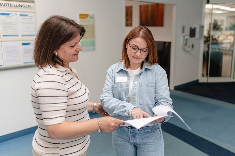 Patientenmanagerin erklärt einer Patientin anhand von Paperdokumtenten wichtige Abläufe