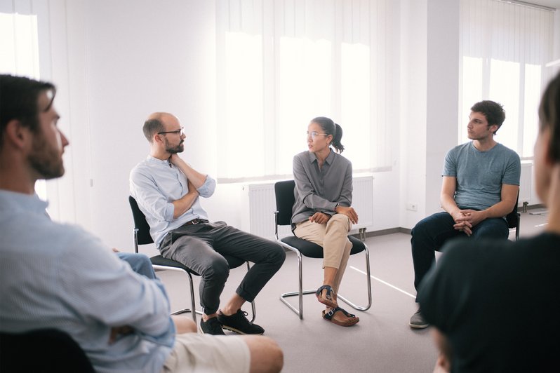 Gruppentherapie - Mehrere Menschen sitzen in einem Stuhlkreis