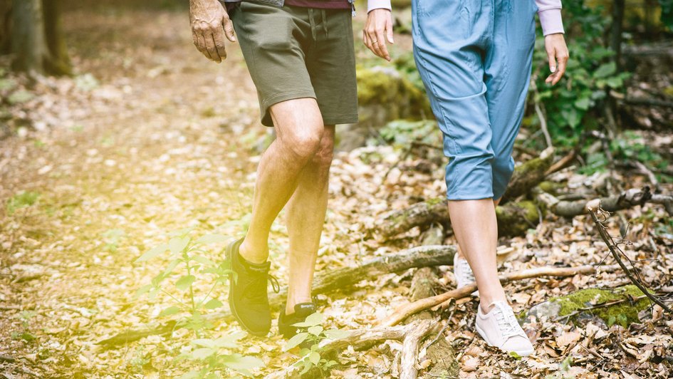Mann und Frau gehen durch den Wald, zu sehen sind nur die unteren Körperhälften.