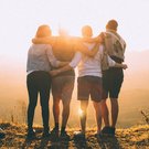 4 Personen stehen Arm-in-Arm nebeneinander und schauen in die Ferne