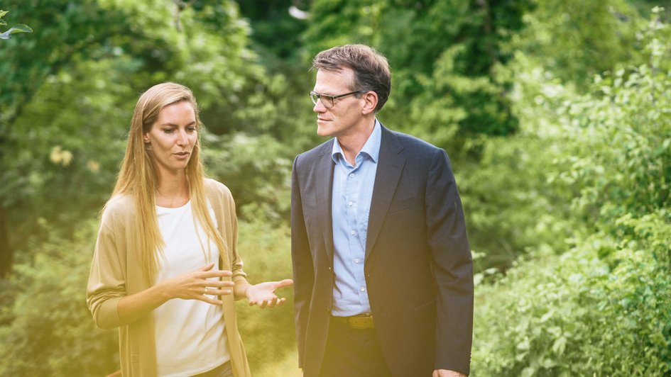 Eine Frau und ein Mann gehen in der Natur spazieren und unterhalten sich.