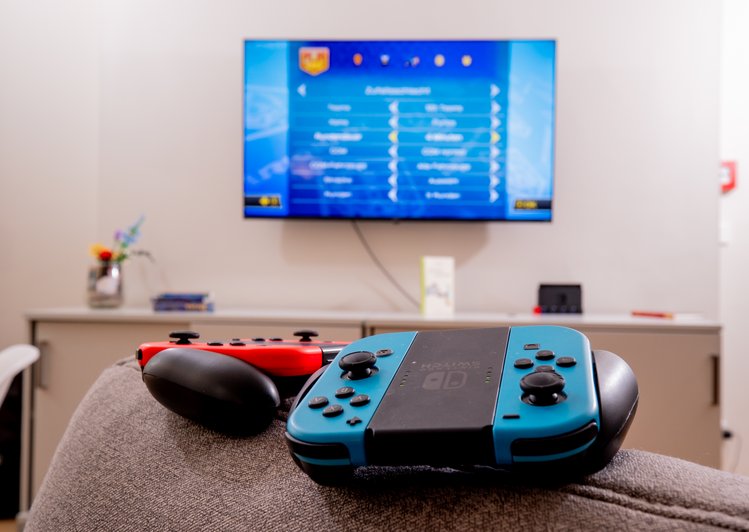 Switch Controller auf Sofa, Fernseher im Hintergrund