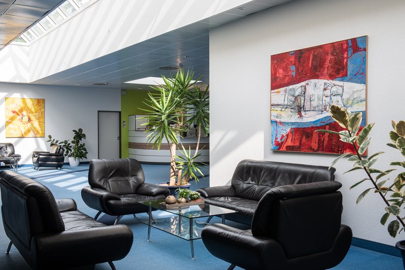 stilvoll gestalteter Empfangs- und Wartebereich mit bequemen Ledersesseln, natürlicher Beleuchtung und farbenfroher Kunst