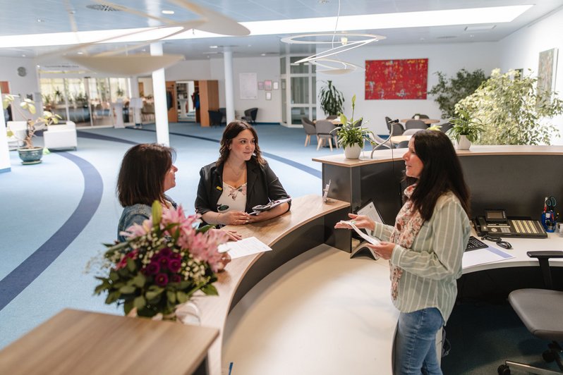 Mitarbeiterin und Patientinnen stehen am Empfangsbereich und unterhalten sich