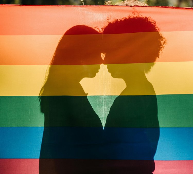 Schattenbild zweier Frauen die sich küssen, versteckt hinter einer Regenbogenfahne