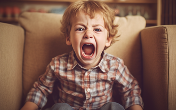 kleiner Junge mit kariertem Hemd sitzt im Sessel und schreit laut