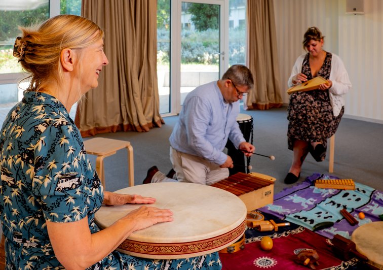 3 Personen sitzen zusammen mit vielen Musikinstrumenten und probieren sich aus.