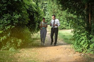 Mann und Frau spazieren auf einem Waldweg nebeneinander her und unterhalten sich.