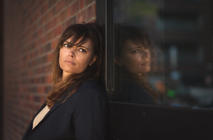 Frau lehnt sich an Backsteinwand, Spieglung in Glasscheibe