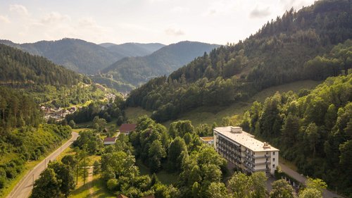 Kastenartiges Gebäude aus der Vogelperspektive in Mitten von bewaldeten Bergen.
