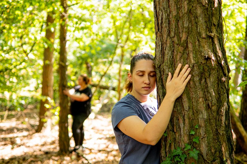 Frau lehnt sich mit dem Kopf gegen einen Baum und hält ihn fest