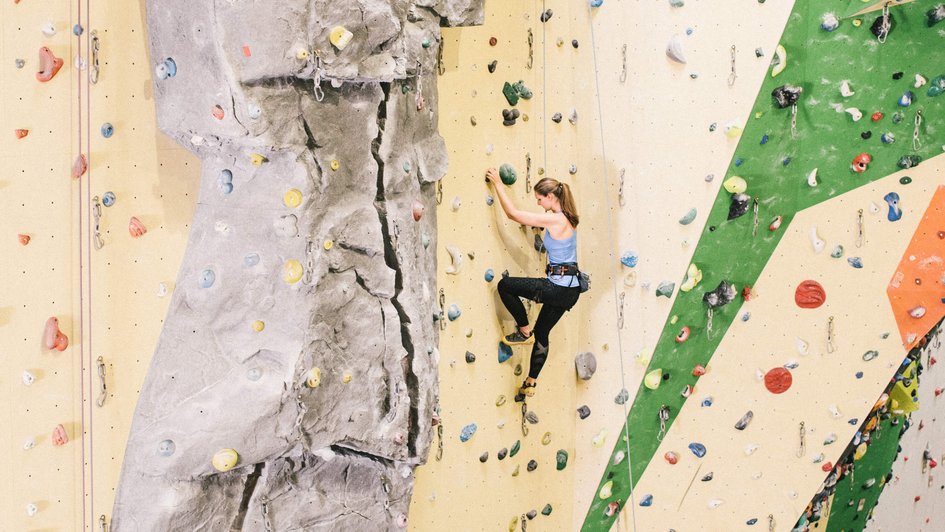 Frau klettert an einer Kletterwand.