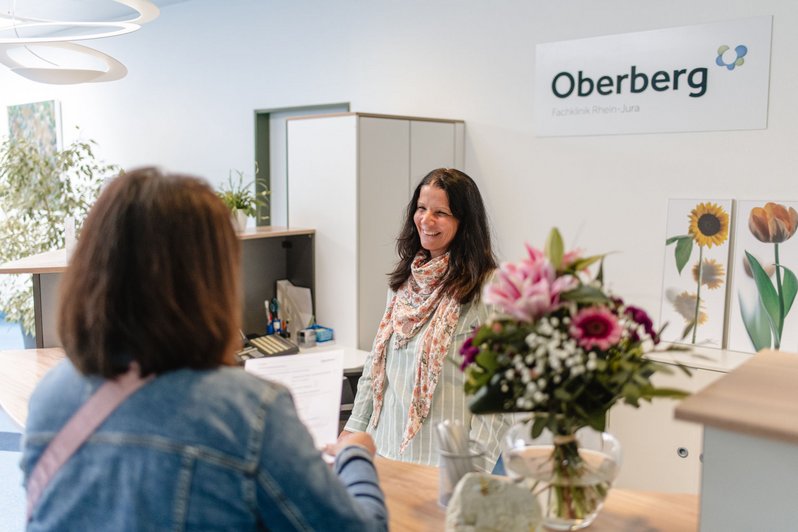 Mitarbeiterin und Patientin unterhalten sich während der Aufnahme am Empfangstresen