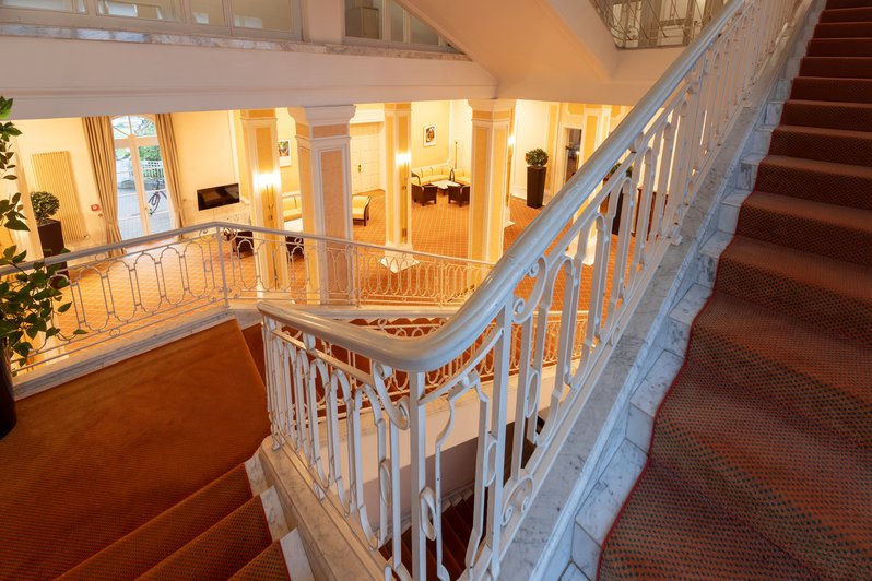 Ambiente der Parkklinik, Treppe mit rotem Teppich hinunter zum beleuchteten Erdgeschoss