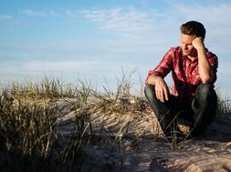 Foto eines Mannes mit rot kariertem Hemd, sitzt auf Sanddüne 