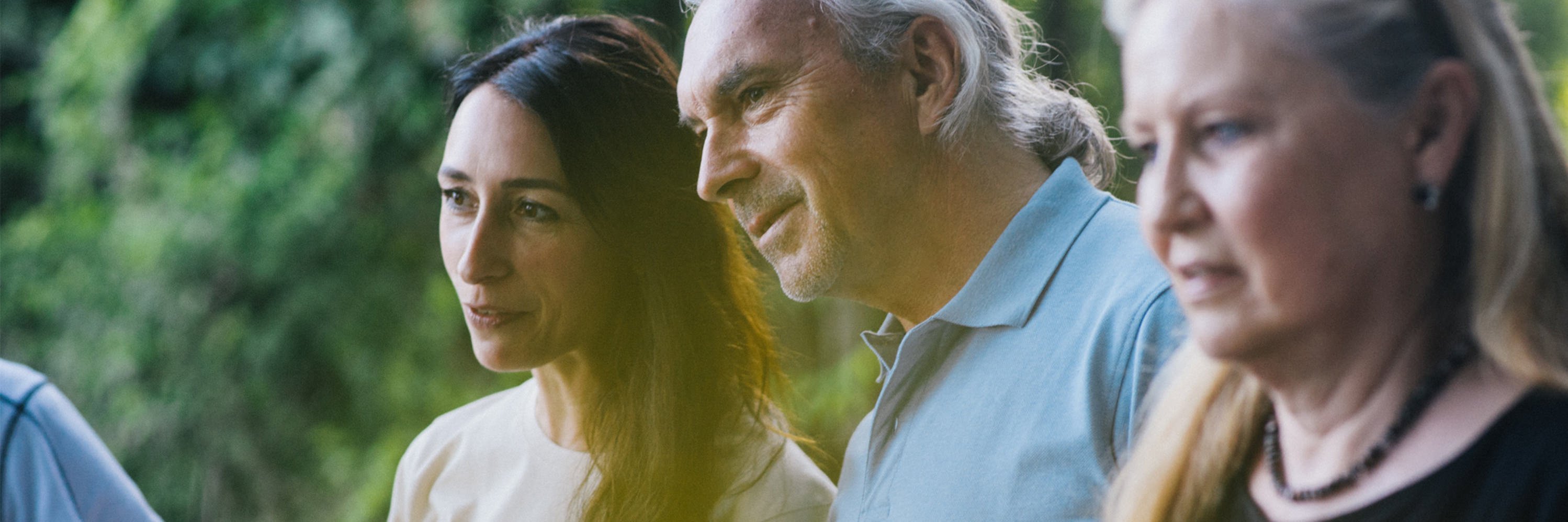 Zwei Frauen und ein Mann stehen in einer Gruppe zusammen, im Hintergrund Bäume.