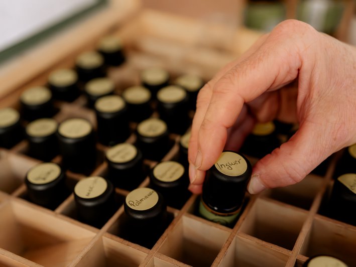 Eine Hand nimmt ein Ingwer-Aromafläschen aus einem Holzkasten