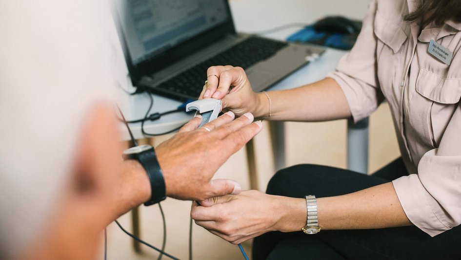 Eine Ärztin steckt einem Patienten einen elektrischen Pulsmesser-Clip an den Finger.