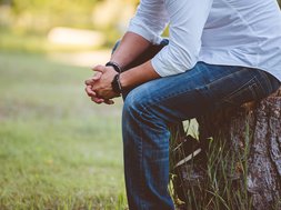 Bipolar - Mann in Jeans und Hemd sitzt auf einem Baumstamm