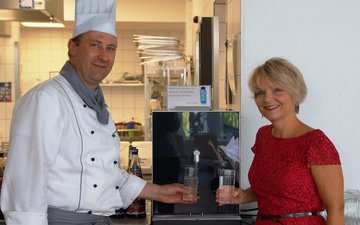 Artikel Trinkwasserspender: Koch und Frau vor einem Trinkwasserspender