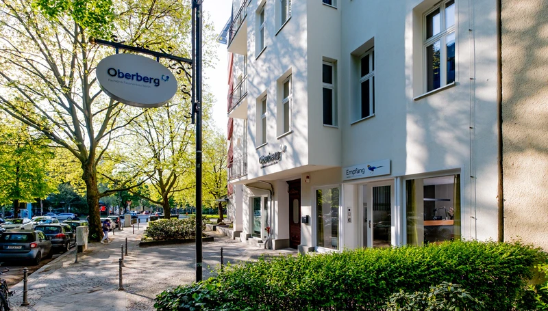Eingangsbereich der Oberberg Fachklinik Fasanenkiez Berlin mit Geb&auml;udefassade, Empfangsbereich und Klinik-Schild an einer begr&uuml;nten Stra&szlig;e